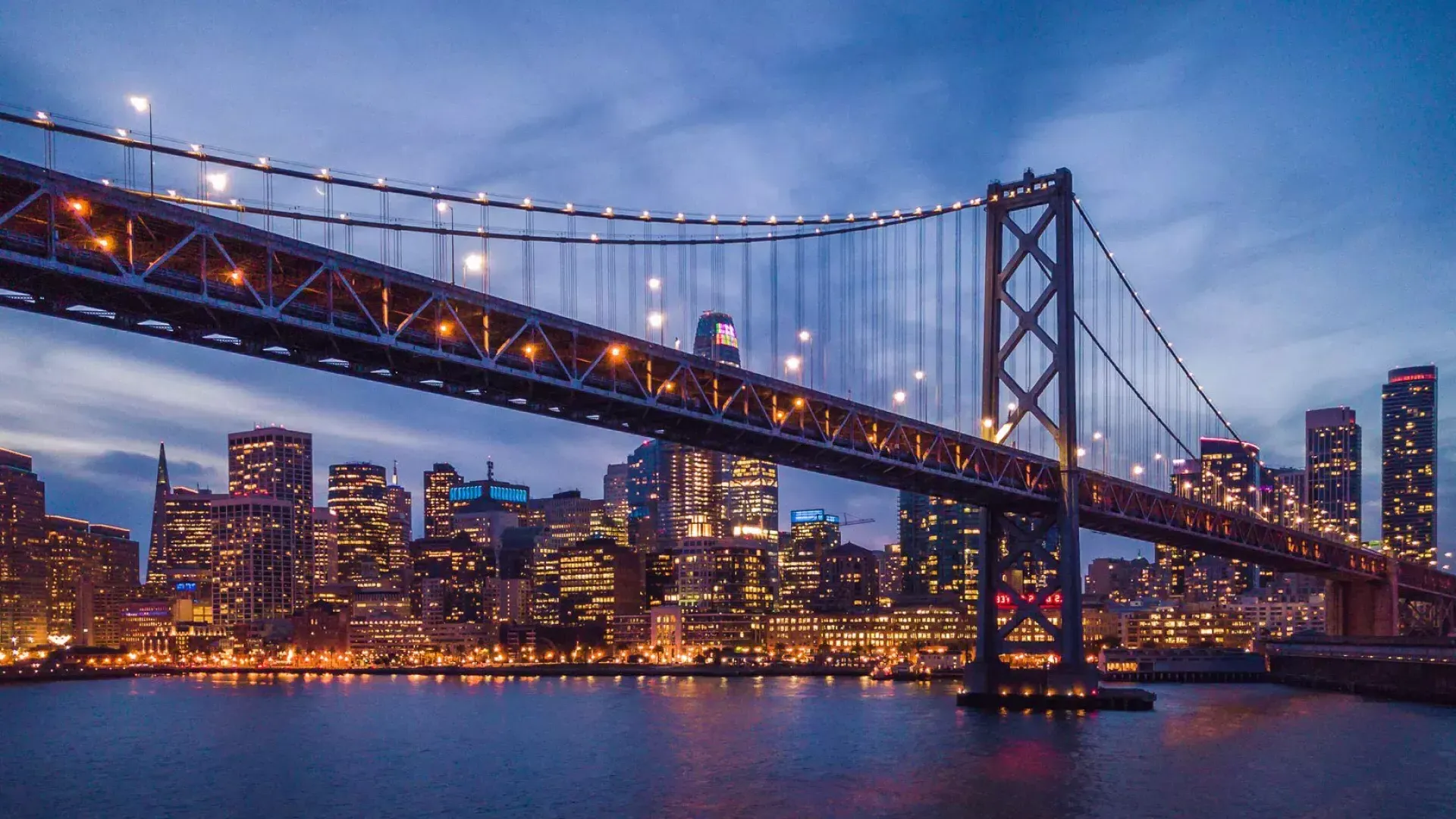 The Bay Bridge and Embarcardero waterfront lit up at night.